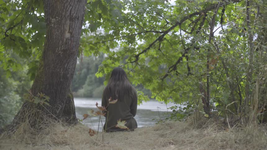 A person sitting at a riverside during the day