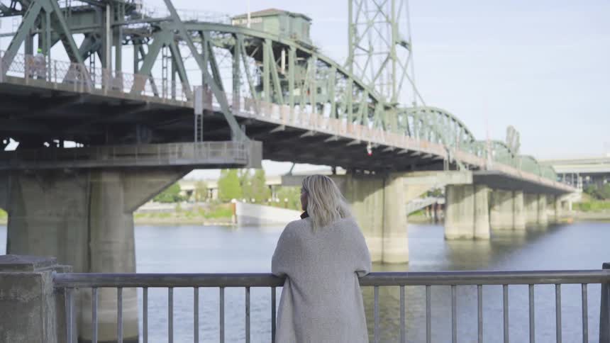A woman by a river looking at a bridge
