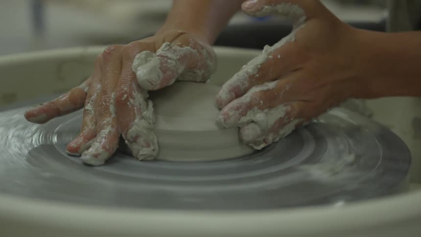 Persons hands mold clay on pottery wheel