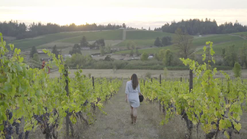 A woman carrying a hat walking through a field