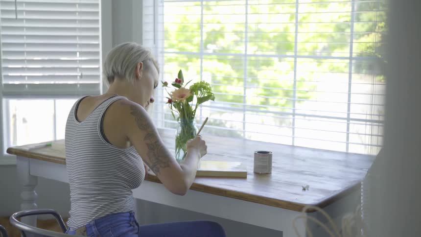 Woman paints a canvas at a table before a window
