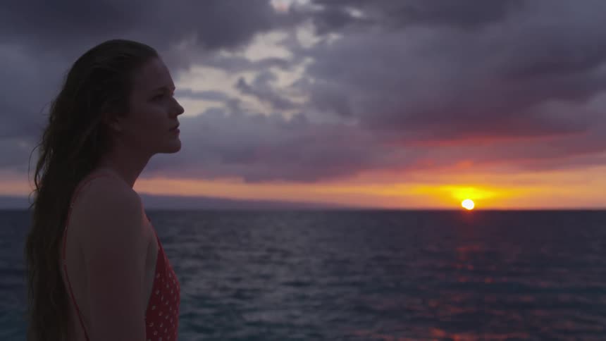 A woman stares across the ocean at dusk