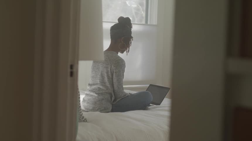 Woman sits on a bed looking at a laptop