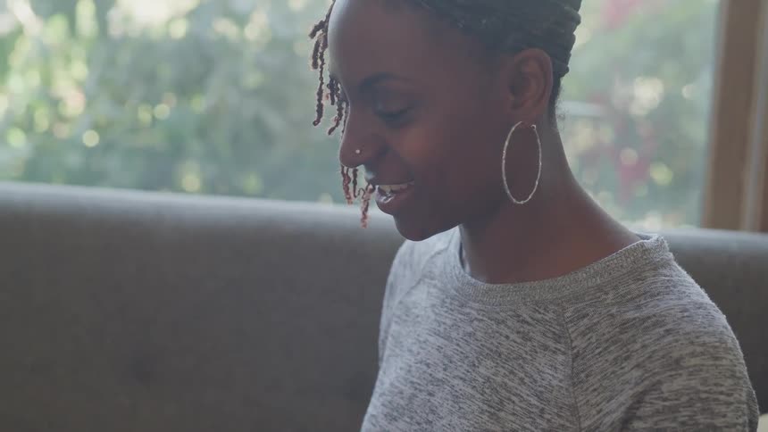 Woman in gray shirt sitting on couch looking down