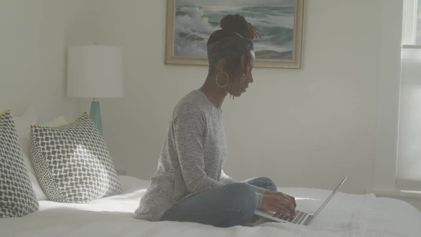 Woman sitting on a bed typing on her laptop