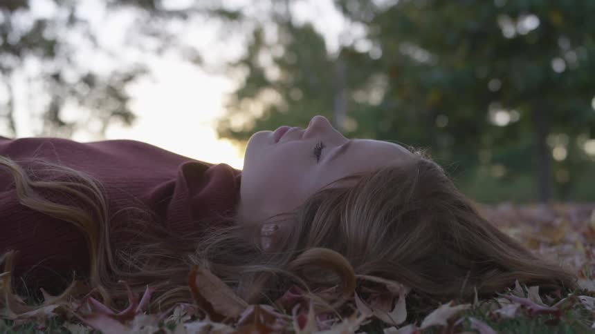 Woman lays on bed of fallen leaves in forest