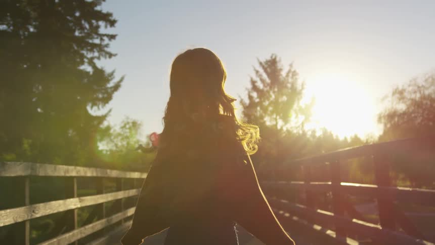A woman spins with a smile while on a wooden bridge in the forest