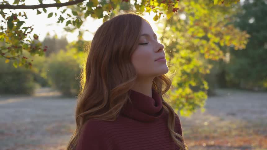 A young woman meditates while standing under a tree with falling leaves