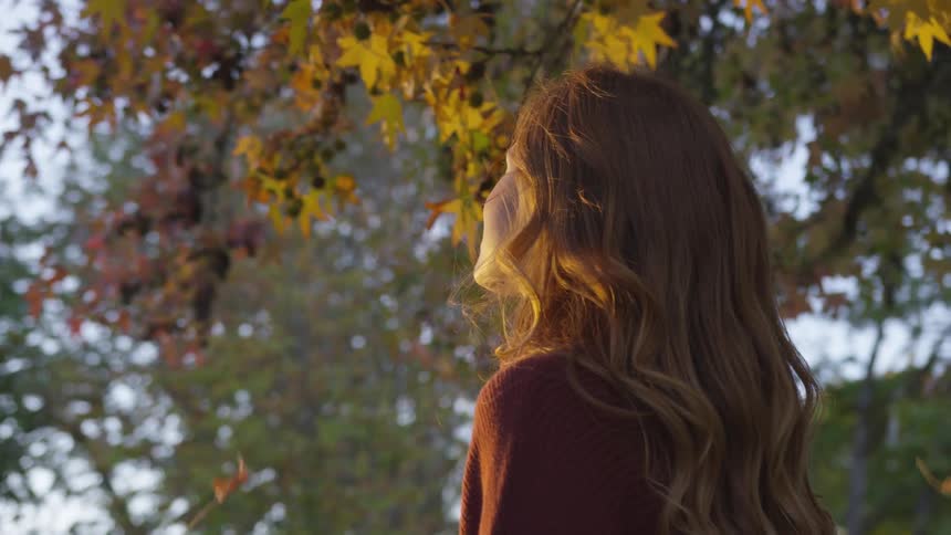 Woman looks up to falling leaves