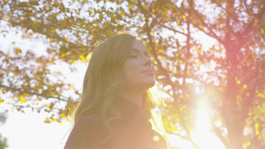 A young woman stands outside with her eyes closed