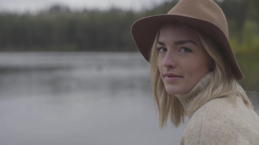 Woman turns to look at the camera sitting near a lake