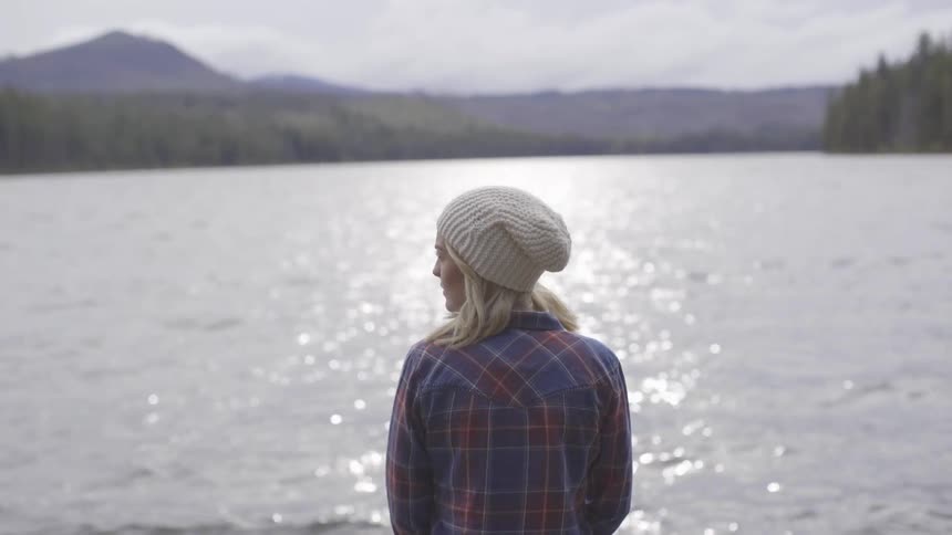A woman stands at the edge of a tree and mountain lined lake