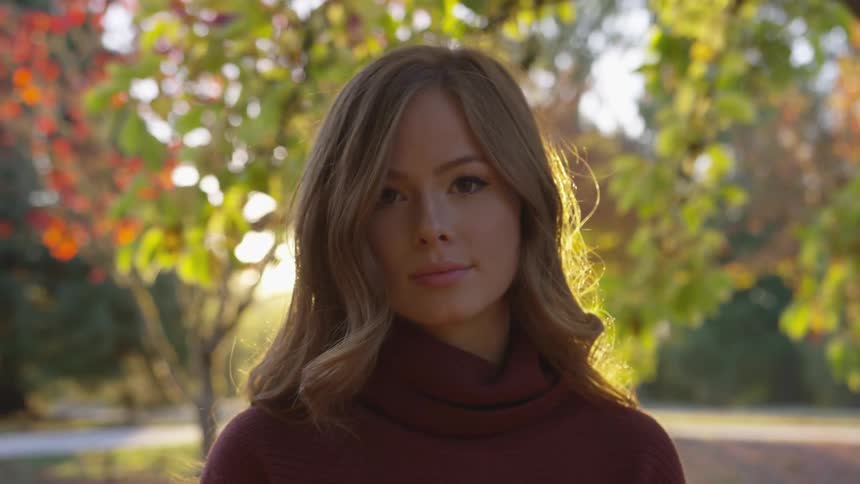 A woman stares into the camera surrounded by fall trees