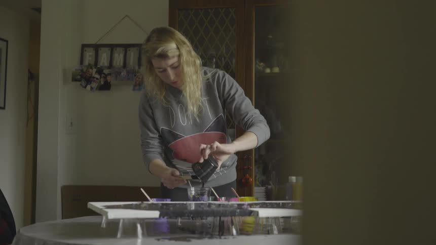 A blonde woman mixes paint at a kitchen table