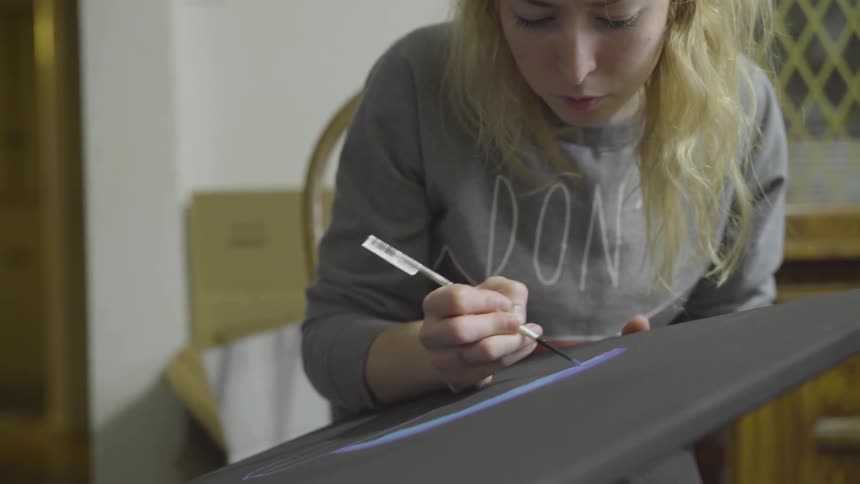 A blonde woman paints on a black canvas