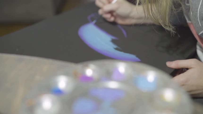 A woman mixing paint and drawing on a black canvas