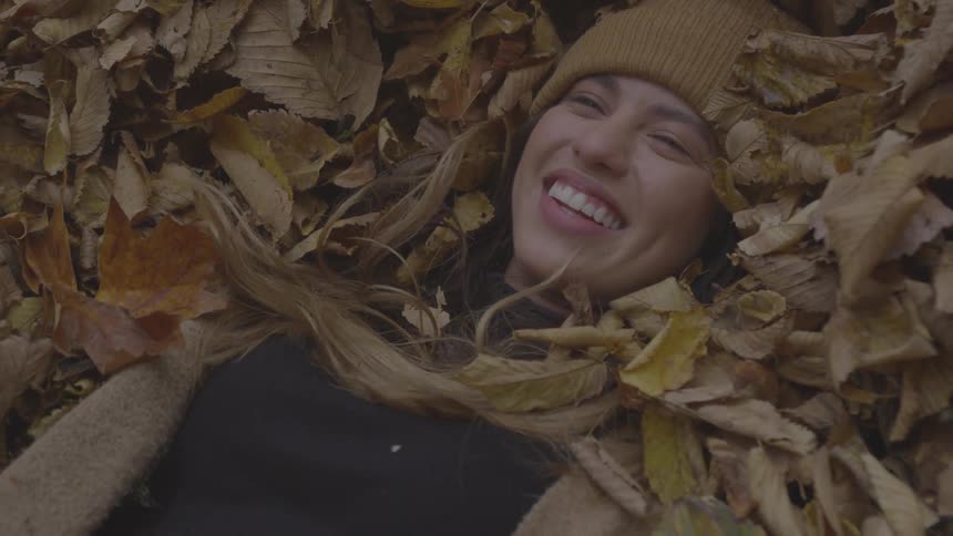 A beautiful blonde white woman smiles while lying in a pile of dead leaves