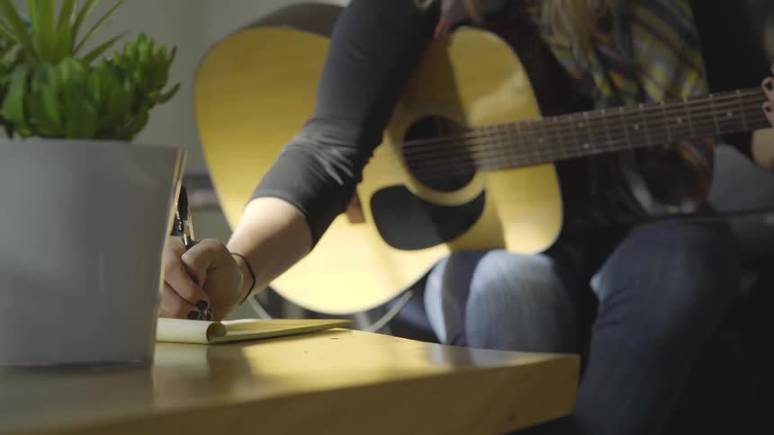 Person plays guitar then makes a not on a pad of paper