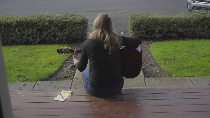 Back view of woman playing guitar sitting on steps outside building
