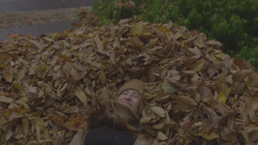A woman falling backwards into a pile of leaves