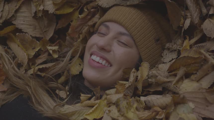 A woman laughs and smiles as she lies in a pile of leaves