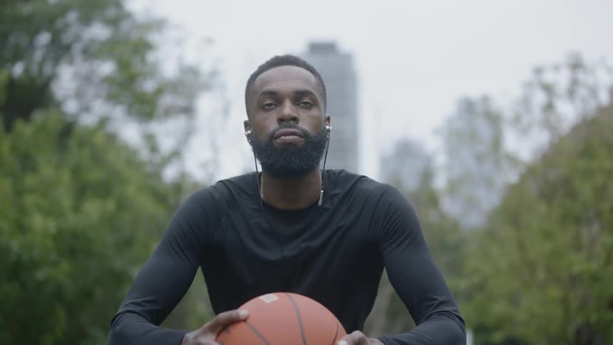 A black man wearing headphones spins a basketball in his hands