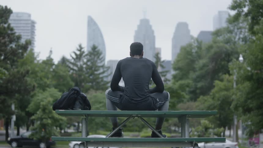A man sits on the table part of a picnic table in a city park