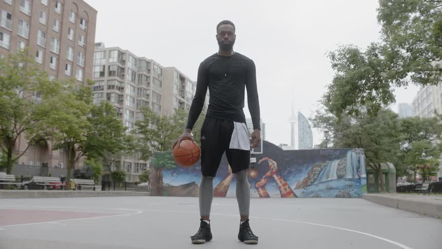 Black man holds a basketball stands in the middle of basketball field in the daytime