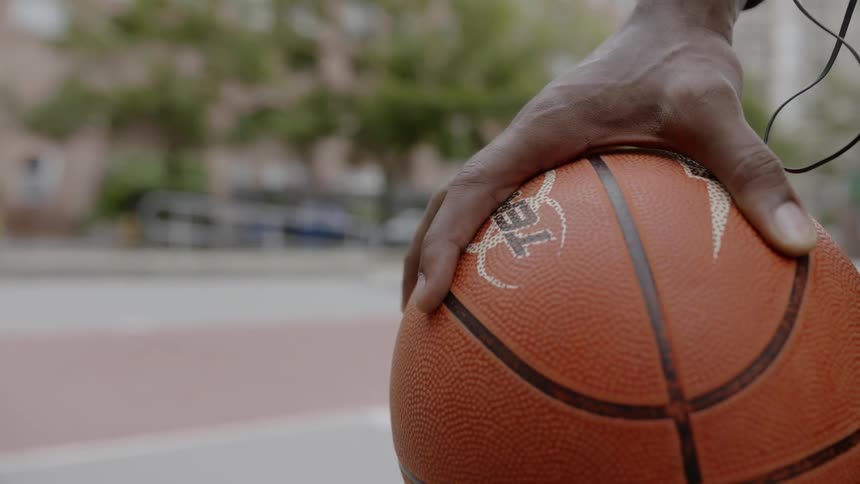 A hand holds a basketball on an outdoor court