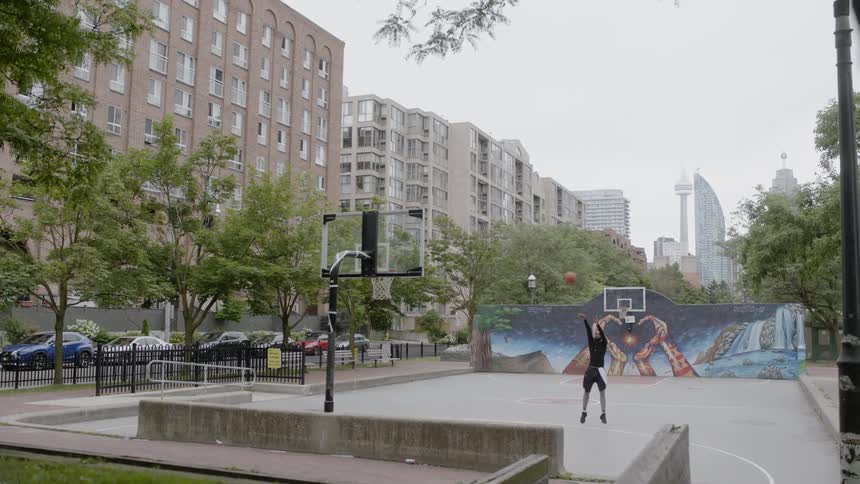 A young black man shoots hoops on an urban basketball court