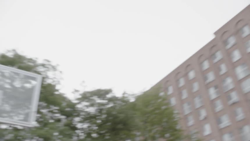 A man with a beard shooting and missing a basket in a city park while wearing headphones