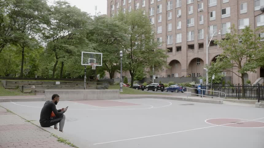 A man sitting at the edge of a basketball court looking through his cell phone