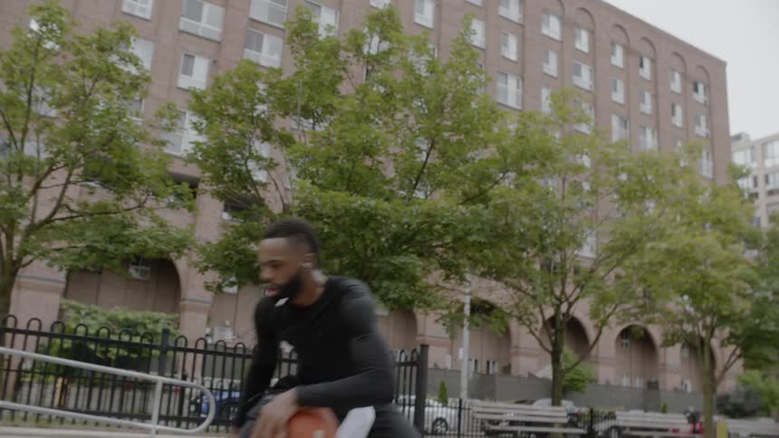 A black man playing basketball in the city