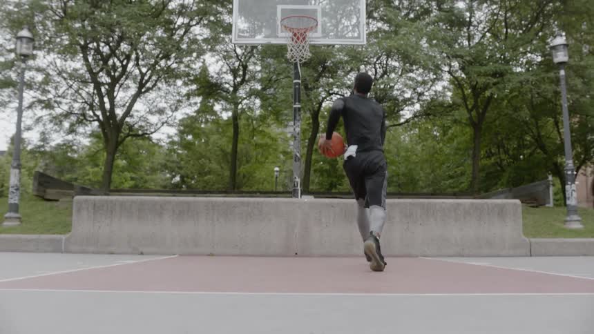 Black man plays basketball in the basketball field in the city on a cloudy day