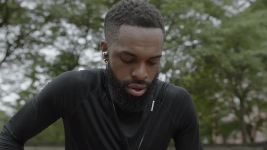 A black man wearing ear buds gets up and walks away
