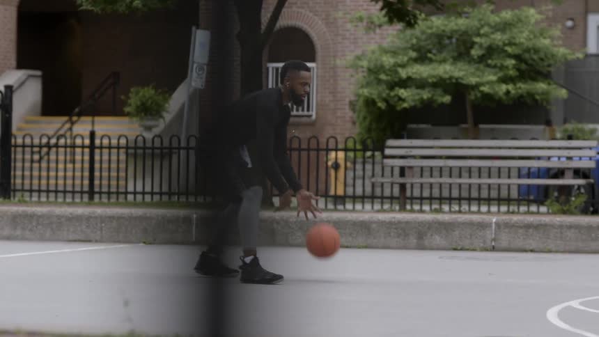 Bearded black man who wears earphones plays basketball in the basketball fiend in the daytime