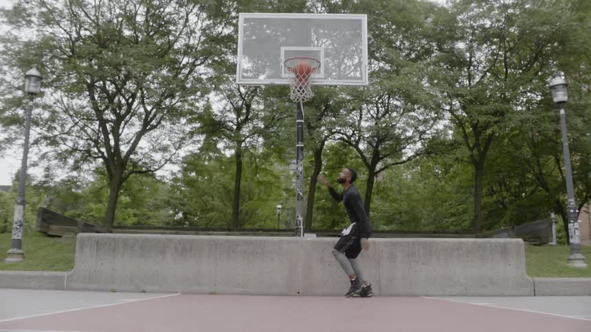 A black male throwing a basketball through a hoop on a basketball court