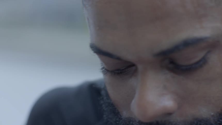 A sweating black man looks around outside and then winces in pain