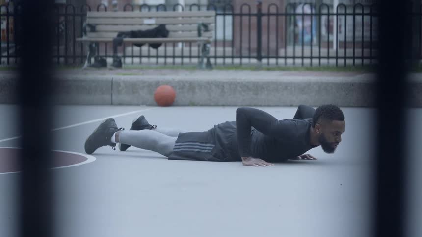 A man stretching on a basketball court near a bench