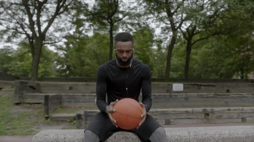 A man sits with a basketball on a concrete slab