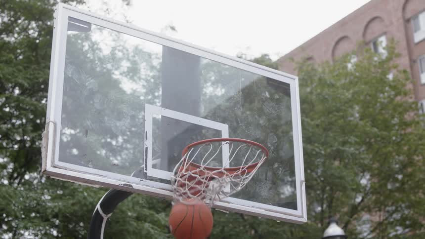 A man jumps and throws a basketball into a basketball hoop on an outdoor court