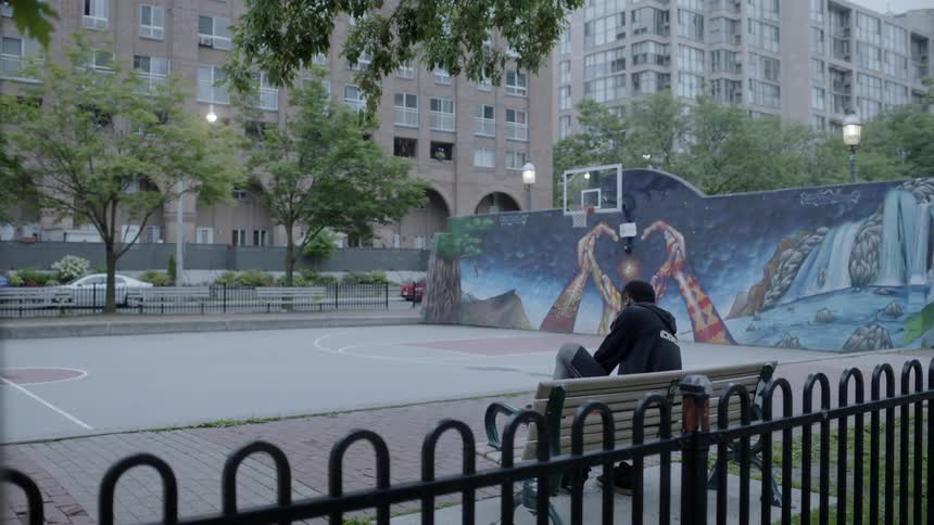 Man sitting on bench near basketball court in a city neighborhood