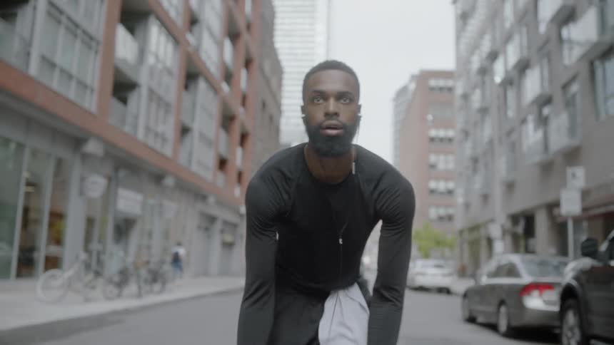 Bearded black man wearing earphones play basketball on the road in the city center