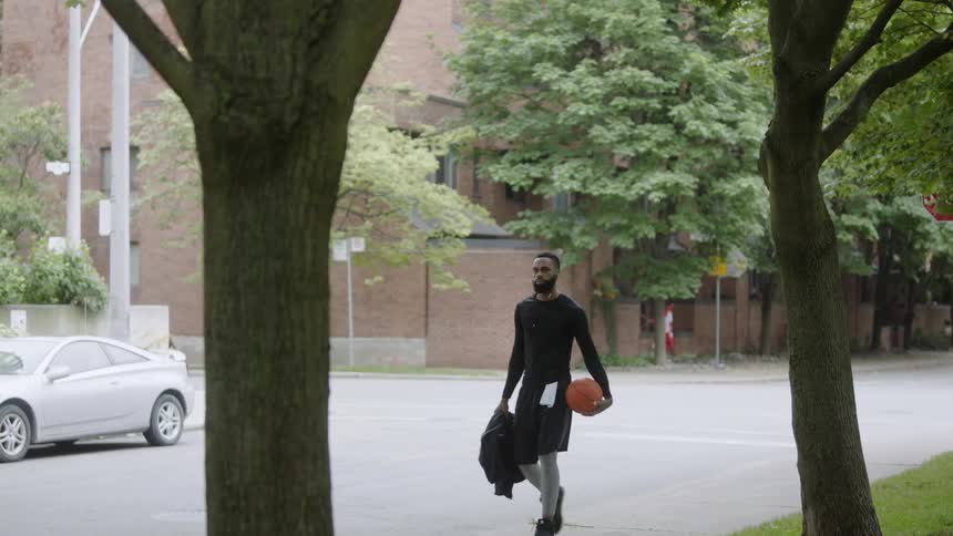 Man walking down side of road carrying basketball and jacket