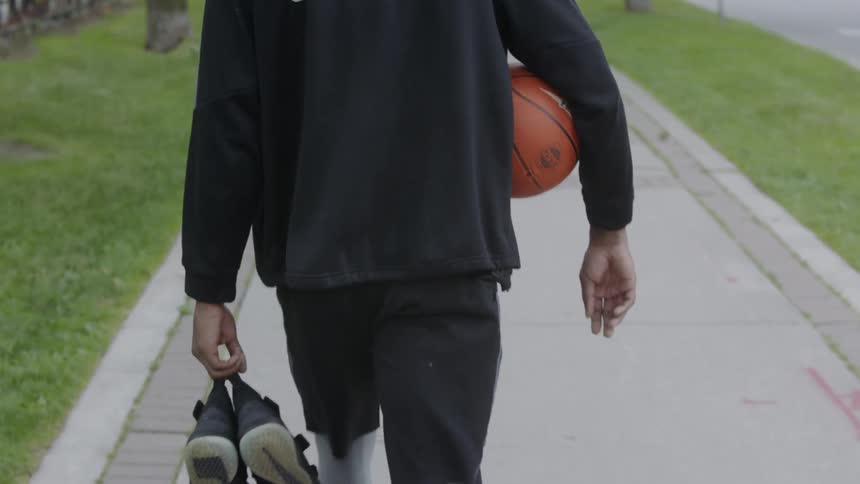 Man walks along sidewalk carrying basketball and shoes