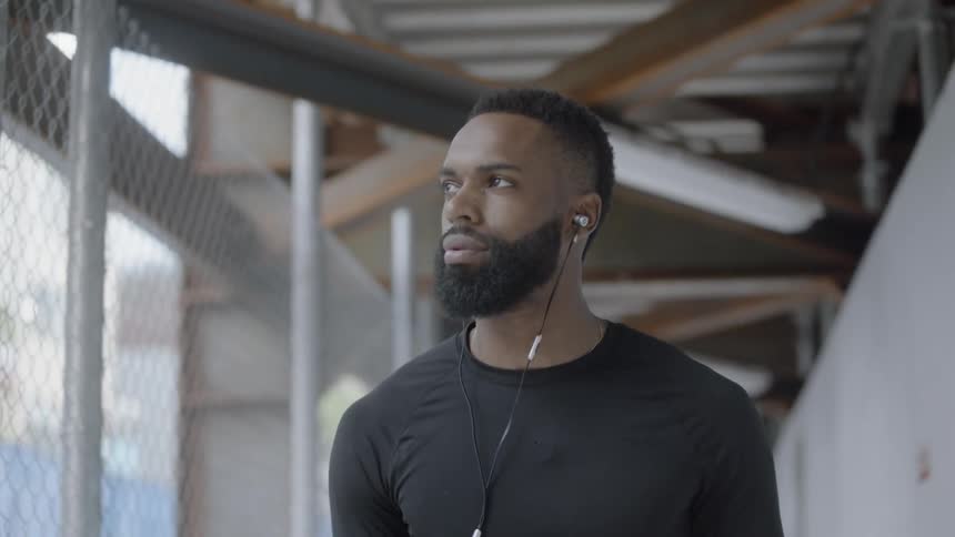 A black man walks down a city path while bouncing a basketball