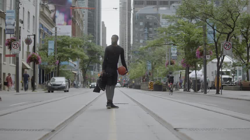 Man in sportswear carrying a basketball crosses the street and stands in the middle