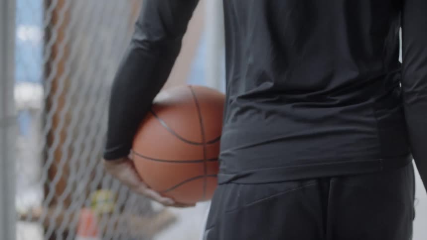 Man walks dribbling basketball past chain link fence