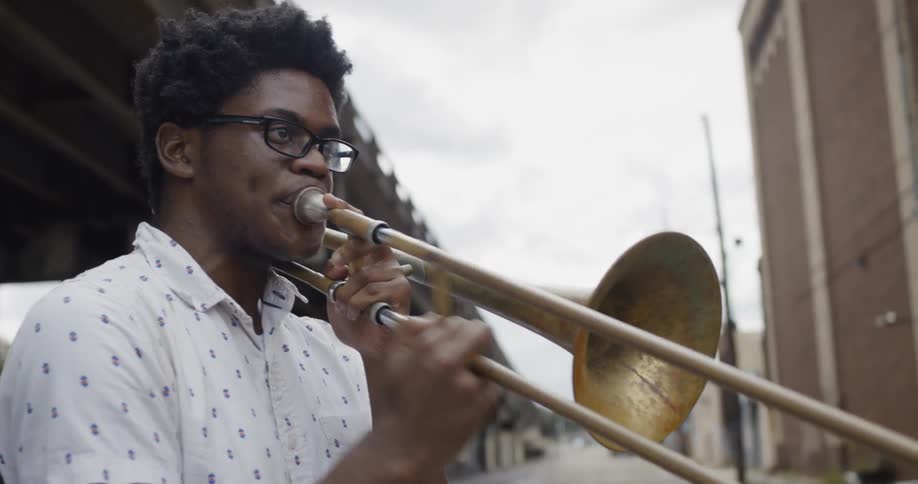 A man plays trombone on the street near a bridge
