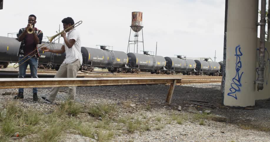 Three boys playing instruments by train tracks